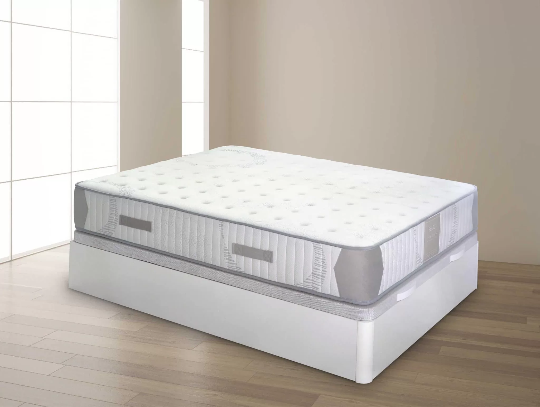 foto de colchón blanco con detalles en color beige sobre canapé blanco. En una habitación de color marrón claro con suelo de madera